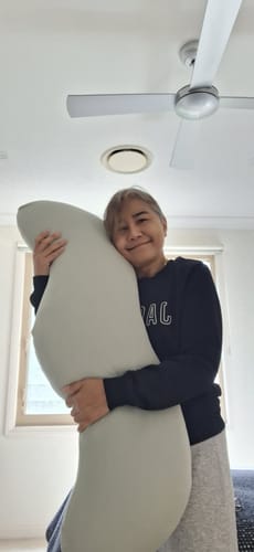 Customer's Snuggi Body Align Pillow, a soft, curved beige pillow held by a person.