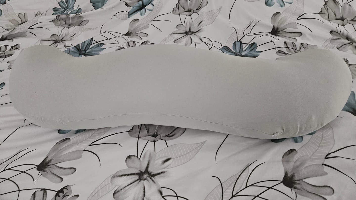 Customer's gray Snuggi Body Align Pillow resting on a floral patterned bedspread.