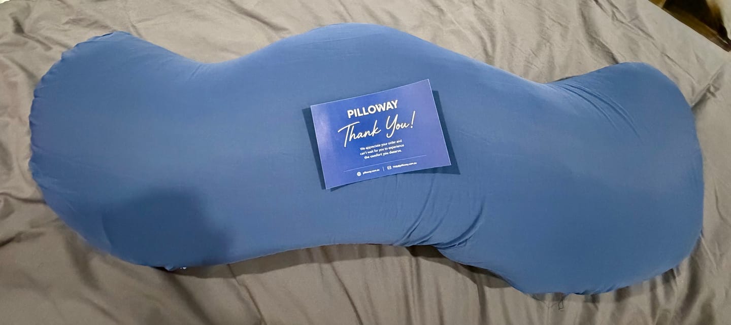 Customer's blue Snuggi Body Align Pillow on a bed with a Thank You note on top.