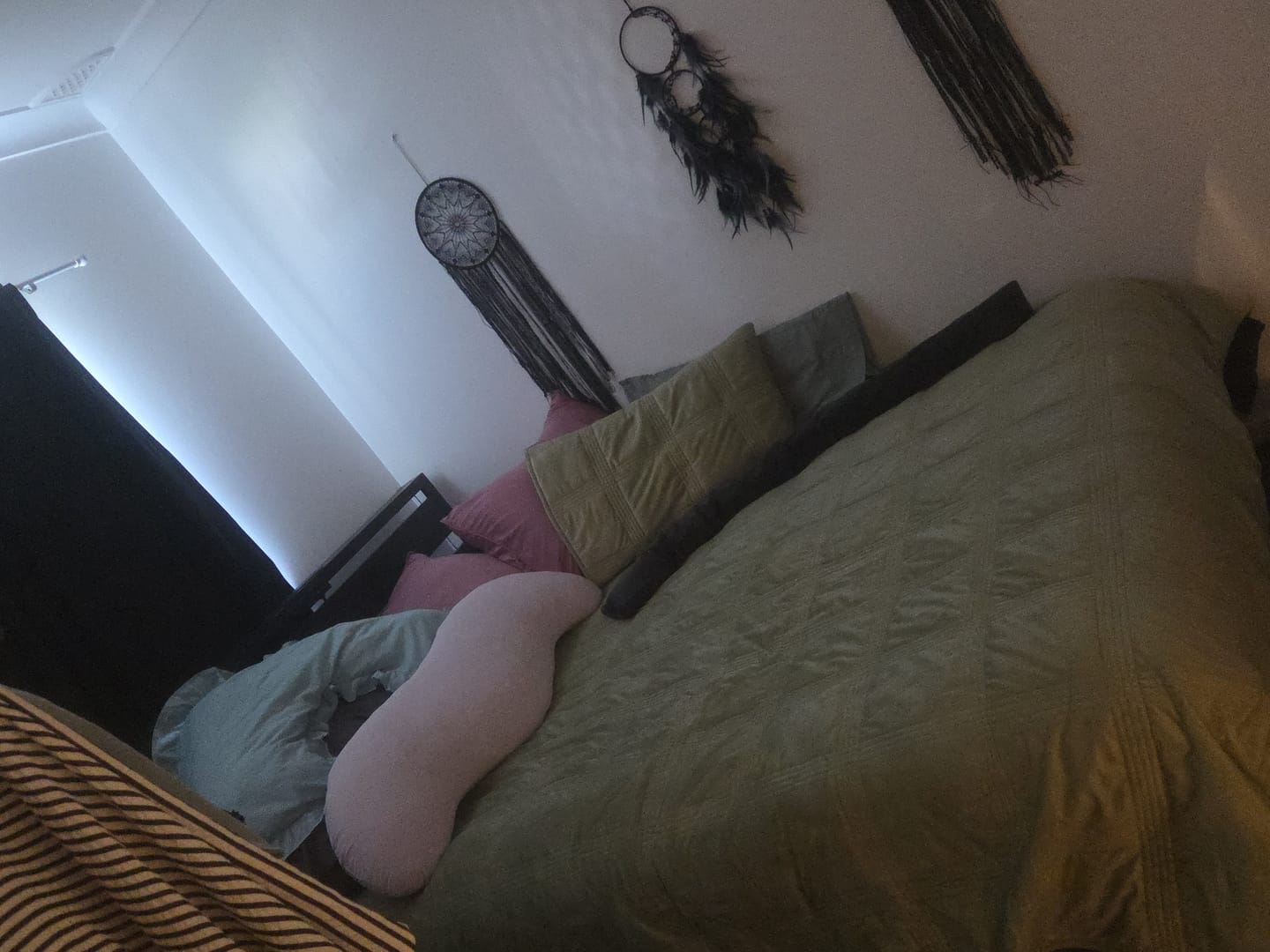 Customer's pink Snuggi Body Align Pillow resting on a green bed in a cozy bedroom.