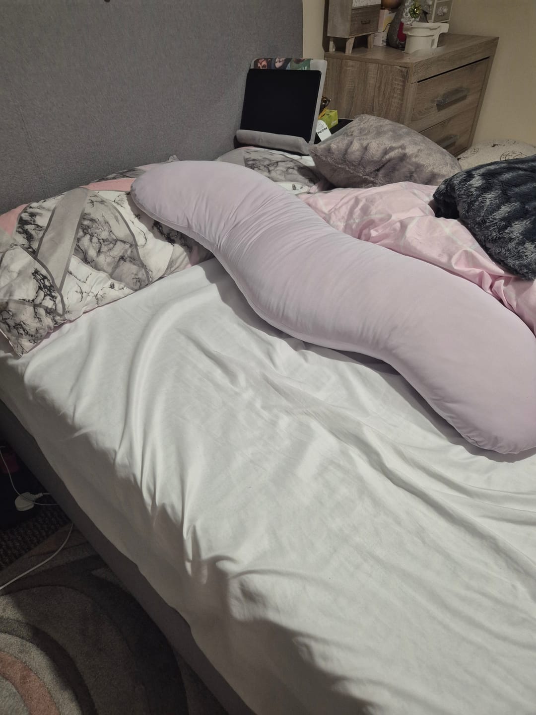 Customer's light purple Snuggi Body Align Pillow resting on a made bed.