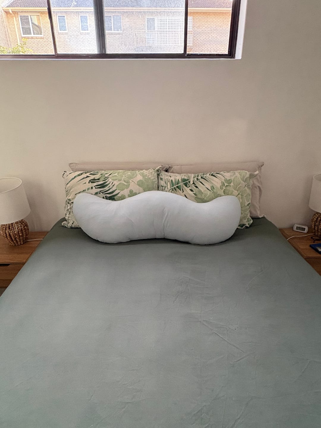 Customer's Snuggi Body Align Pillow sitting on a made bed between green leaf-patterned throw pillows.