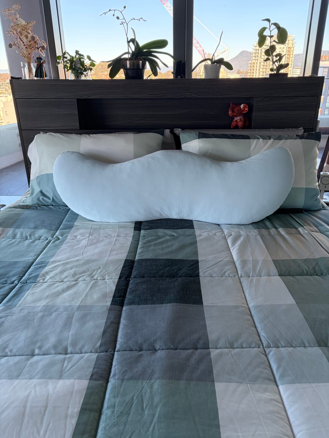 Customer's Snuggi Cooling Pillow Case, a light blue curved pillow resting on a bed with a dark headboard.